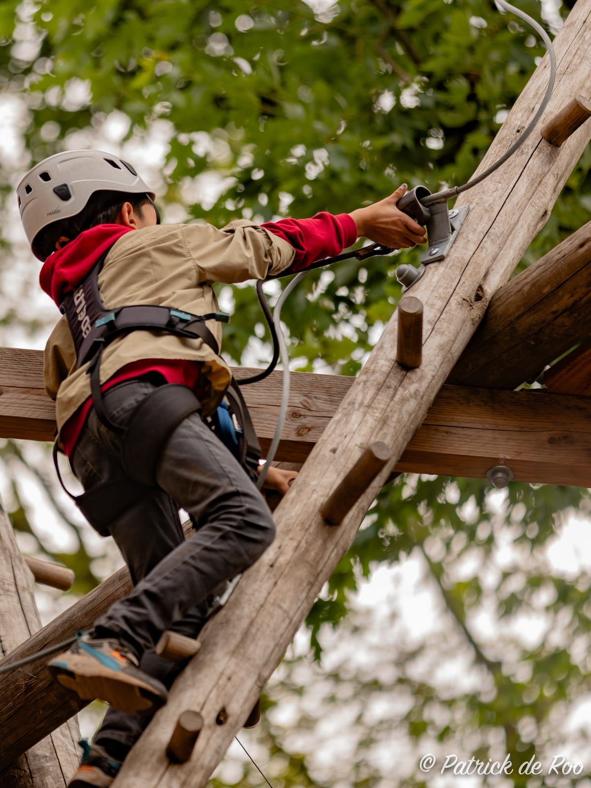 Scout met helm klimt in een zelfgebouwde pionierconstructie tussen de bomen