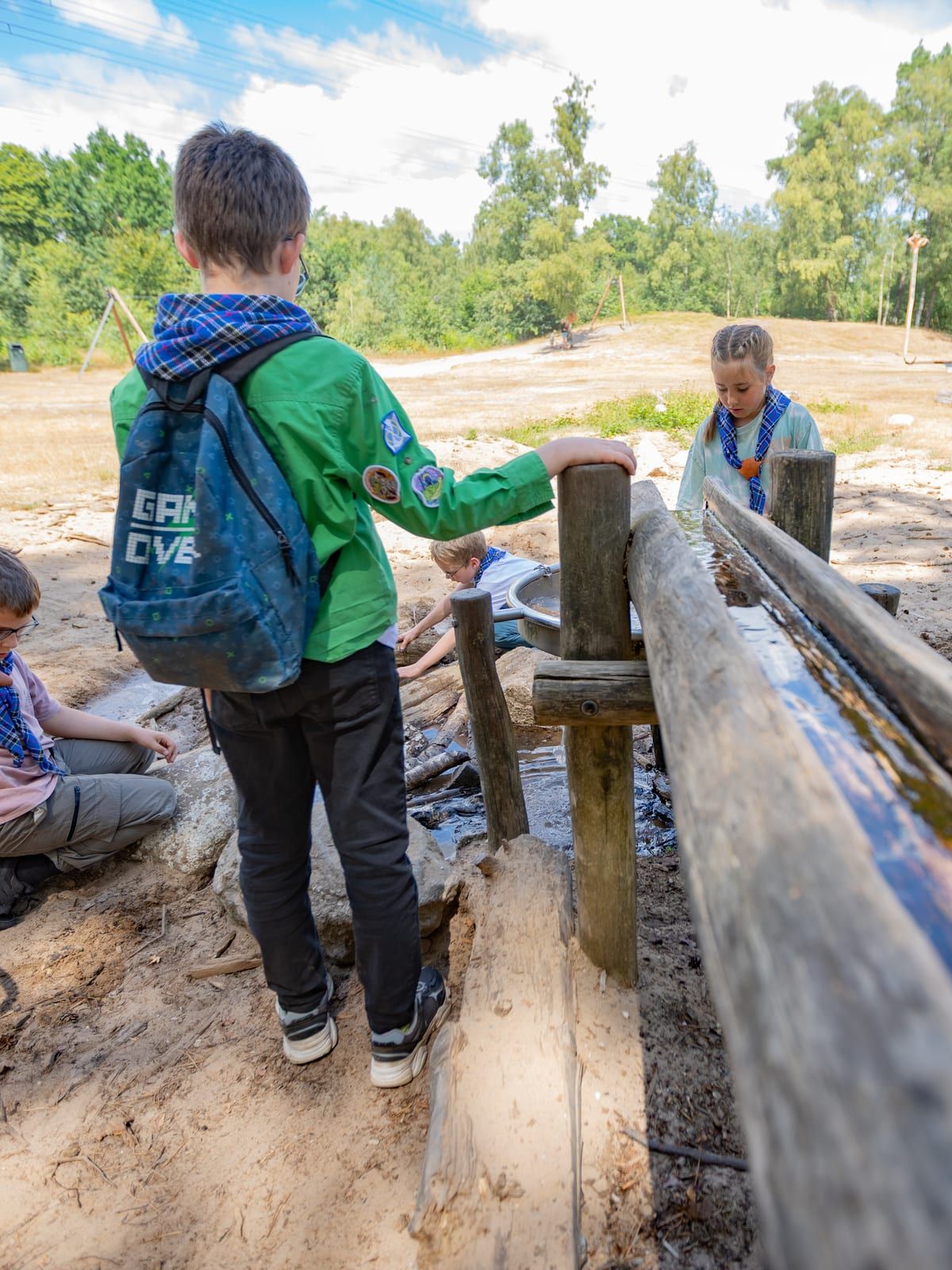 Welp met groene trui speelt bij de waterbaan, met twee andere welpen erbij