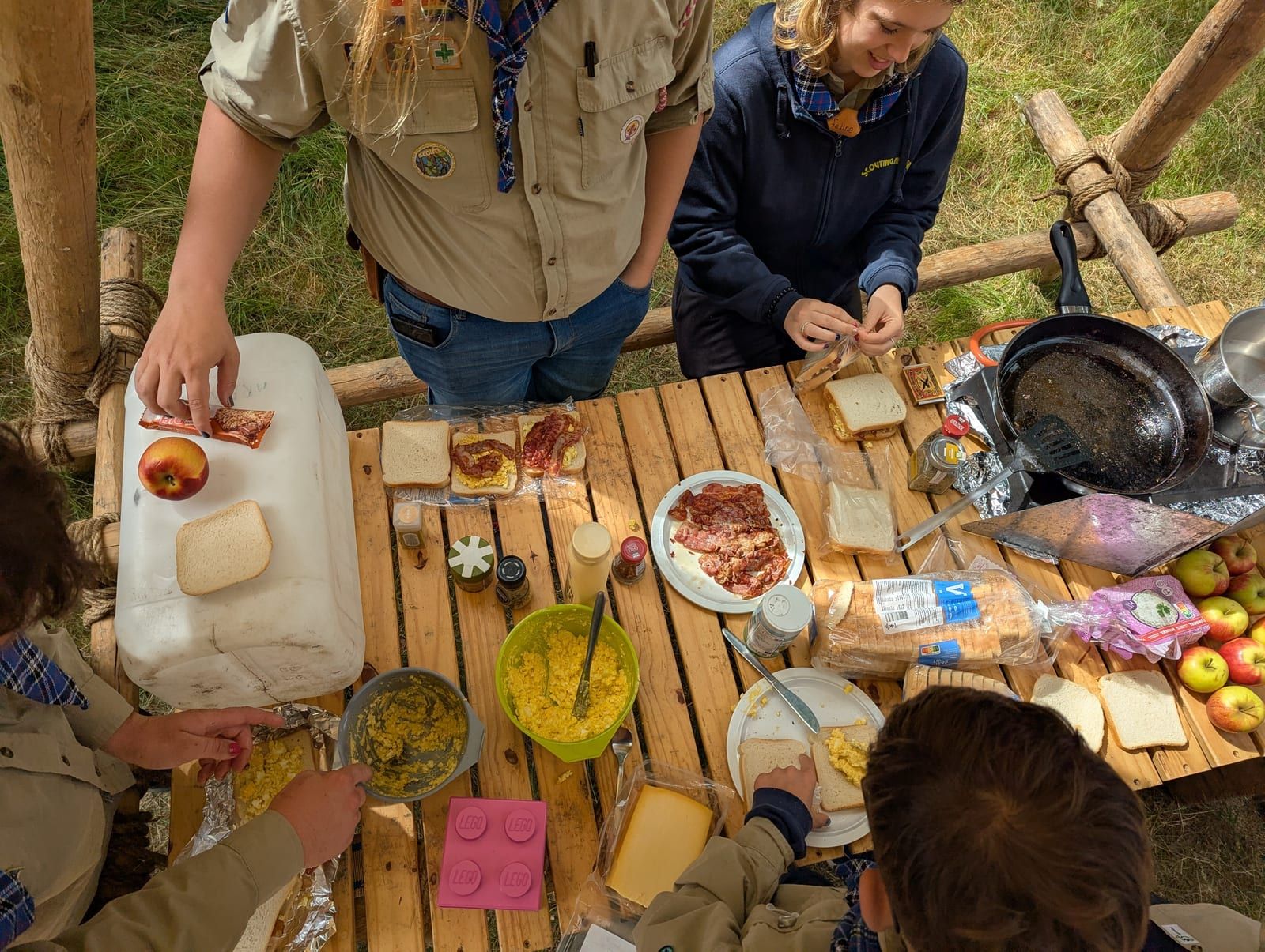 Scouts maken samen eten klaar aan een zelfgebouwde tafel op kamp