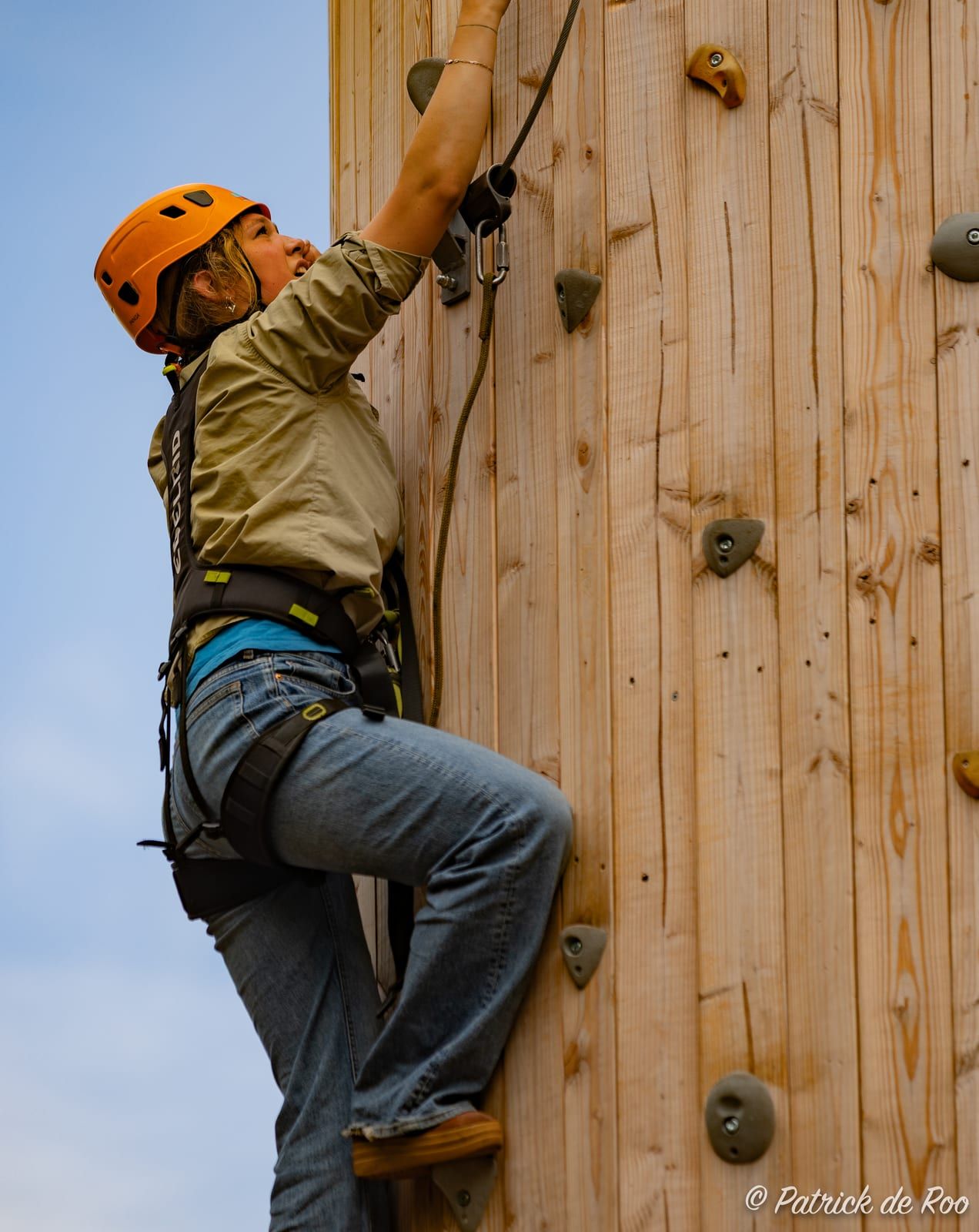 Scout klimt met helm en klimgordel tegen de klimtoren
